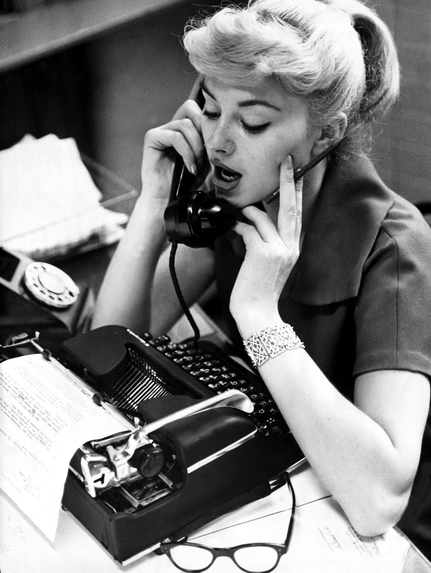 A support agent handling two telephone calls beside a typewriter